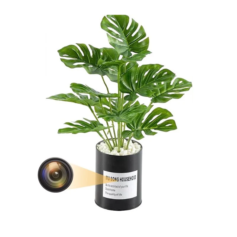 Artificial potted plant with green leaves in a black container labeled "MU SONG HOUSEHOLD"; a discreet hidden camera is depicted inside the pot.